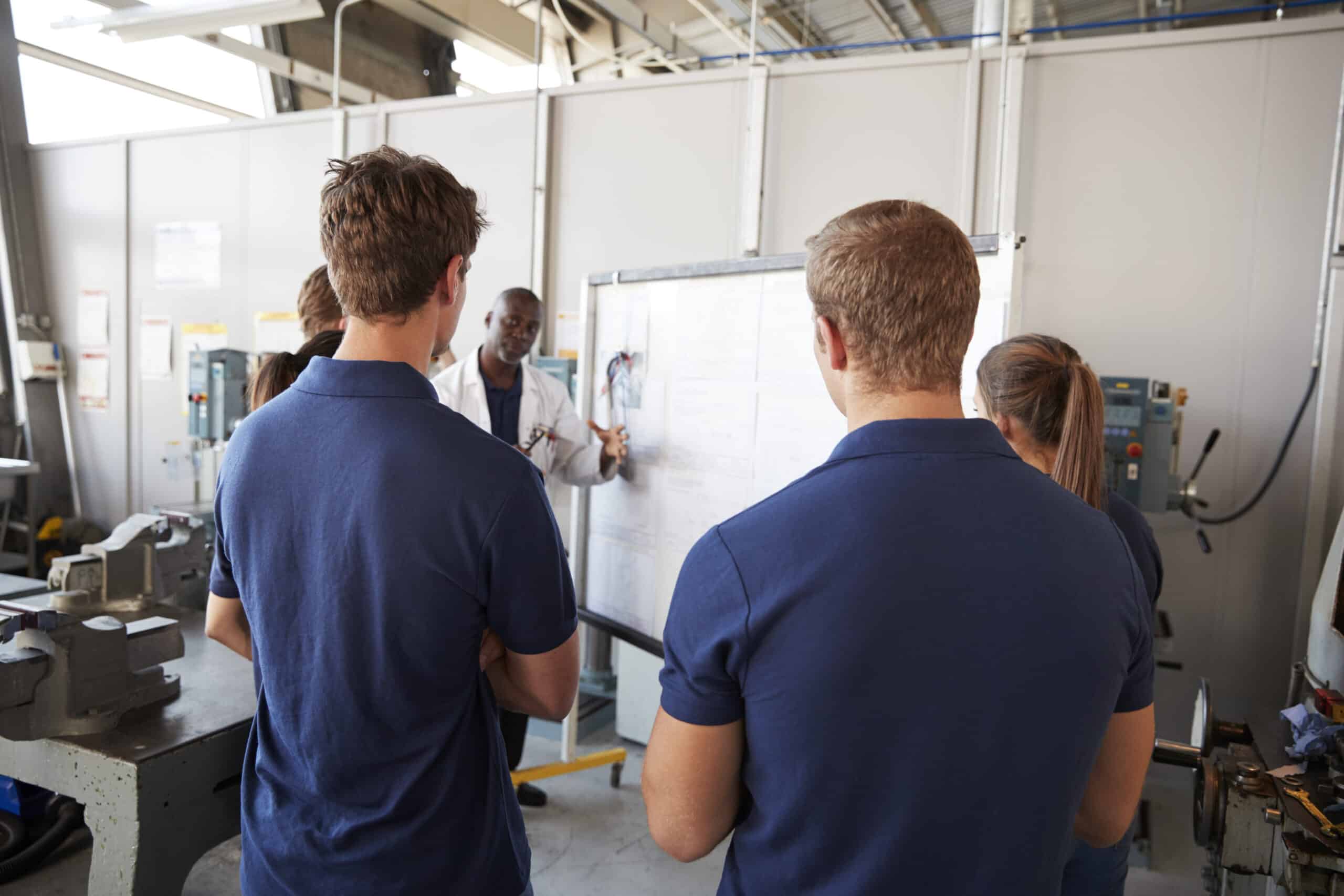 apprentices gathered around a whiteboard in a workshop